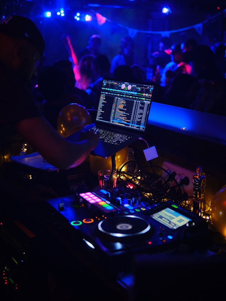DJ aux platines dans un bar de nuit, piste bondée en arrière-plan