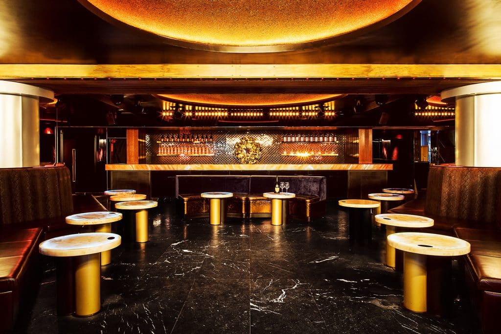 Salon d'un club parisien aux tables dorées et bar rétroéclairé